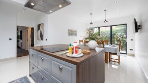 A modern kitchen with a central island, built-in cabinets, and a dining area with a table and chairs. - Modern 4 bedroom Detached House Near Manchester City (Salford)