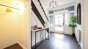 A staircase with a black railing, a white console table with various items, and a door with glass panels and a plant beside it. - Modern 4 bedroom Detached House Near Manchester City (Salford)