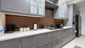 A modern kitchen with grey cabinets, a stainless steel sink, and a built-in oven. There are jars on the counter and a coffee maker. - Modern 4 bedroom Detached House Near Manchester City (Salford)