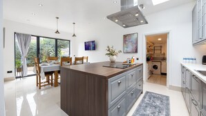 A modern kitchen with a central island, built-in appliances, and a dining area with a view to the outdoors. - Modern 4 bedroom Detached House Near Manchester City (Salford)