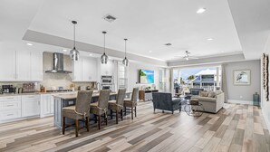 A modern kitchen with white cabinets, a dining area with wicker chairs, and a living room with a sofa and coffee table. - Ocean Pearl Vacation Rental (Fort Myers Beach)