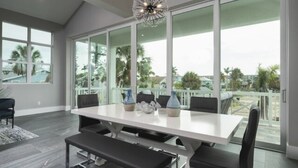 A spacious dining area with a large table and chairs, large windows with a view of palm trees and a deck outside. - Saltwater Fantasea Vacation Home (Fort Myers Beach)