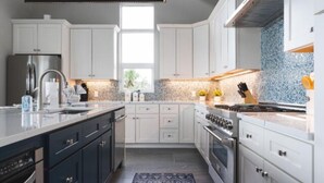 A modern kitchen with white cabinets, stainless steel appliances, and a blue backsplash. - Saltwater Fantasea Vacation Home (Fort Myers Beach)