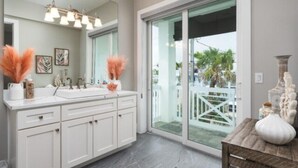 A modern bathroom with a large mirror, dual sinks, and a view of a balcony with a white fence. - Saltwater Fantasea Vacation Home (Fort Myers Beach)