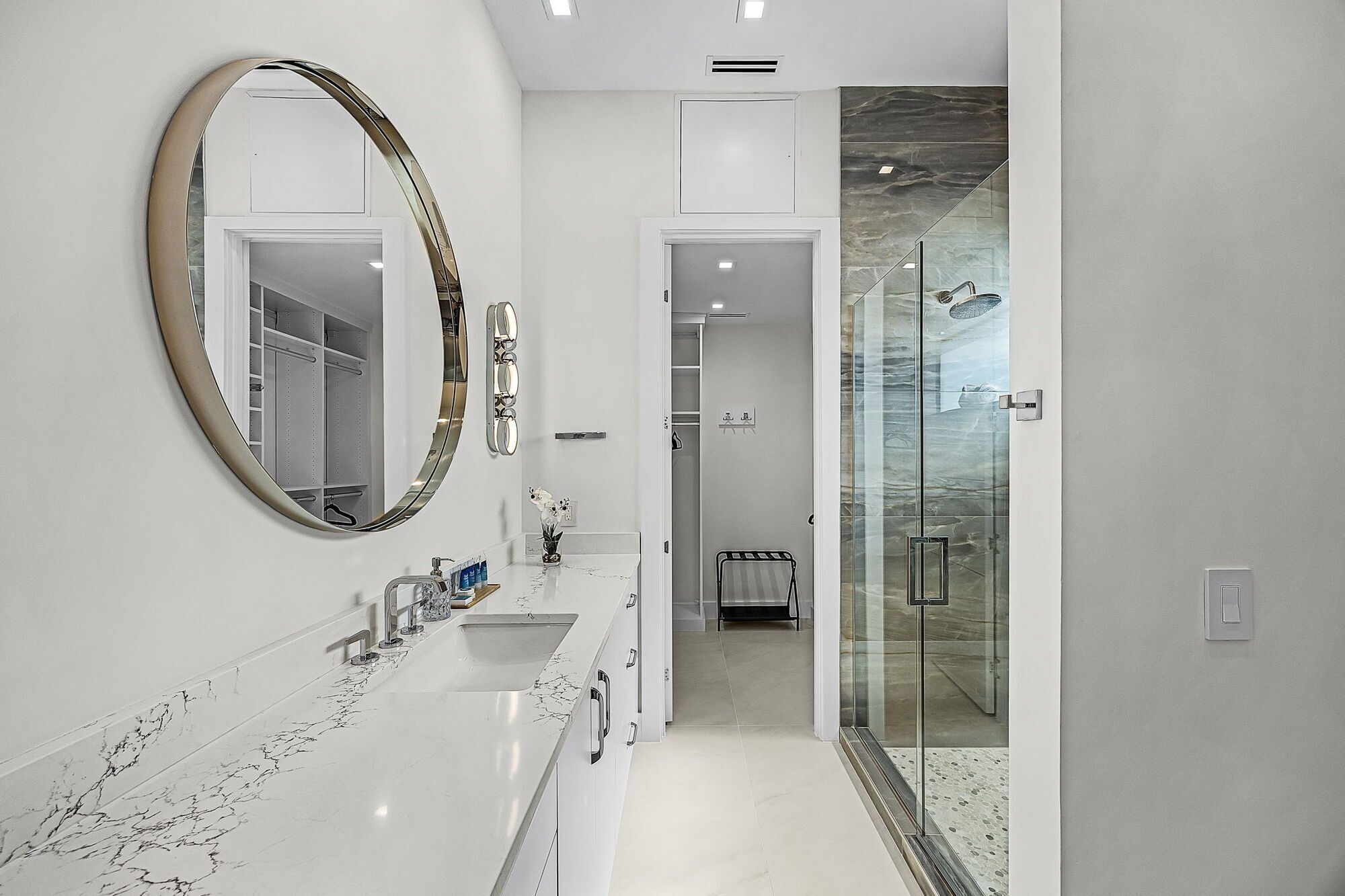 Un baño moderno con un espejo grande, encimera de mármol y cabina de ducha de vidrio.
