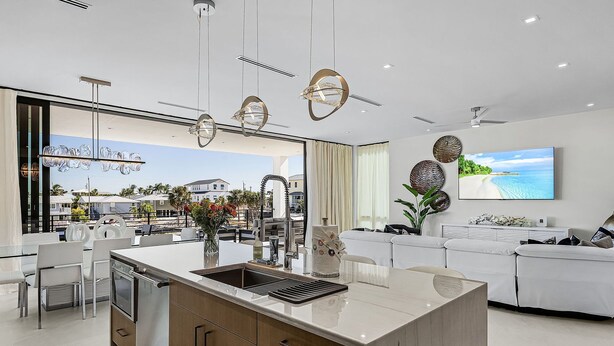 A modern kitchen with a central island, dining area, and a living room with a TV.
