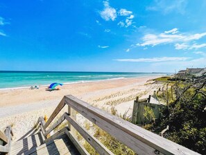 A beach with a wooden walkway leading to the shore, a clear blue sky, and a distant pier.