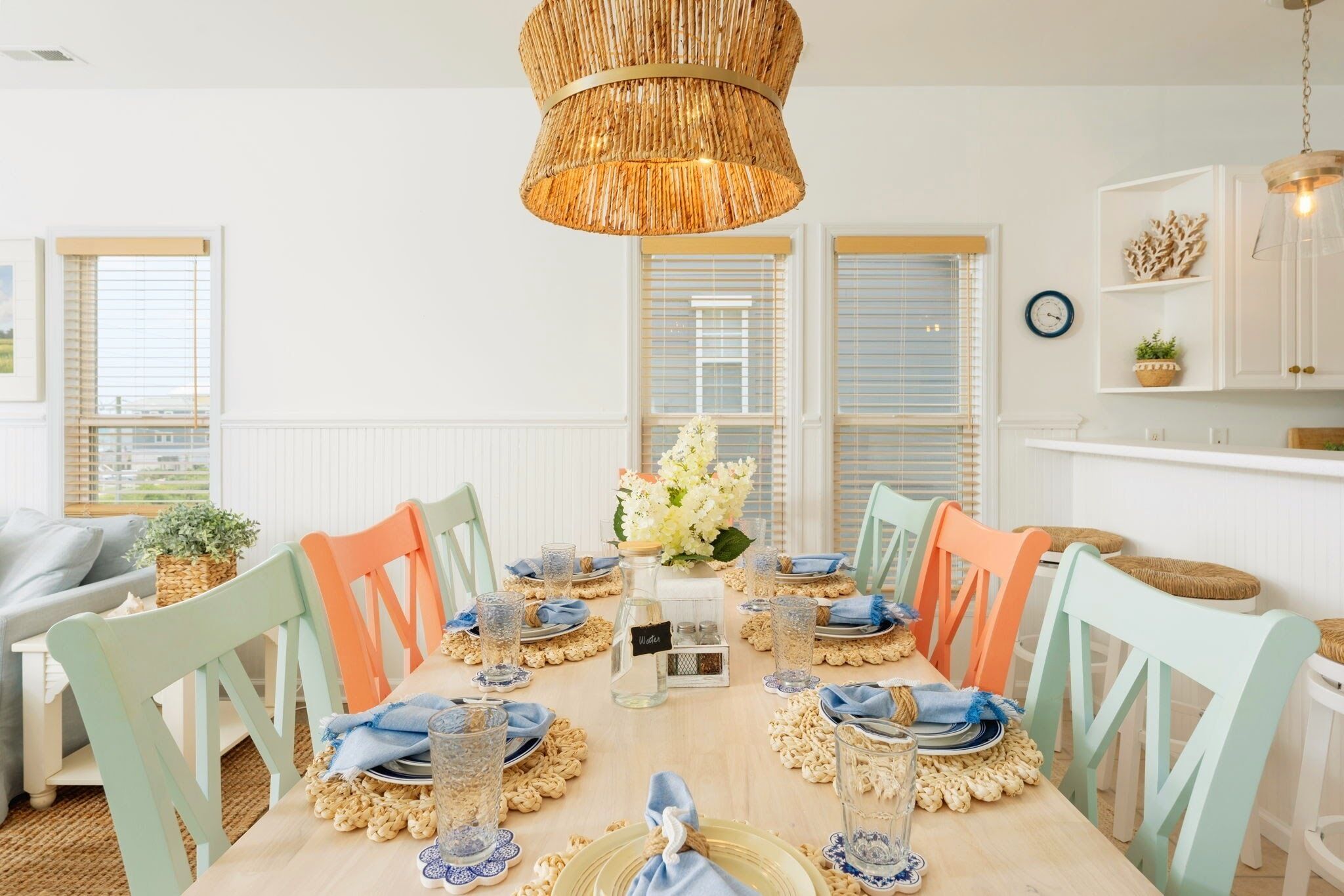 A dining area with a wooden table set for six, surrounded by pastel-colored chairs.