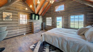 Ein Schlafzimmer in einer Blockhütte mit einem Bett, einem Fernseher und einem Fenster mit Blick auf eine Landschaft.