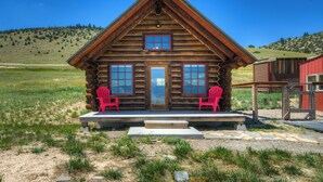 Eine Blockhütte mit Veranda, zwei roten Stühlen und einer Holztür.