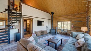 Ein geräumiges Wohnzimmer mit einer großen Couch, einem Couchtisch und einem Kamin. Eine Treppe führt auf eine obere Ebene, und ein Fernseher ist an der Wand montiert.