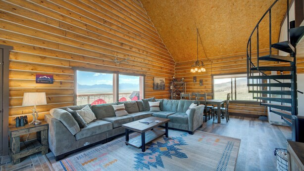 Ein Holzblockhaus-Interieur mit einer großen Couch, einem Esstisch und einer Wendeltreppe.