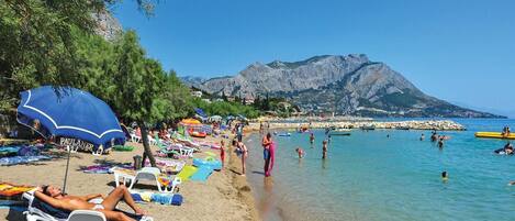 A beach with sun loungers, umbrellas, and people swimming.