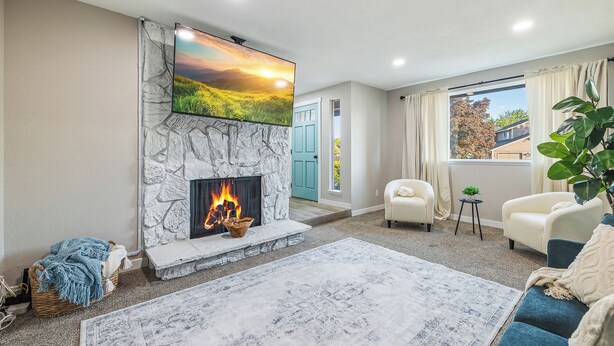 A living room with a stone fireplace, a flat-screen TV mounted above it, a blue sofa, and a large rug. - Sapphire Lodge - 3 bed home in prime of Kennewick (Kennewick)