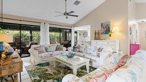 Un salon spacieux doté d’un ventilateur de plafond, de grandes fenêtres et offrant une vue sur la verdure environnante.