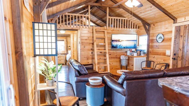 A cozy cabin interior with a wooden interior, a large TV, and a seating area with leather sofas. - Waterfront Retreat for 8 w/Fire Pit, Boat Dock, no steps to water! 3BR/2BA (Cadiz)