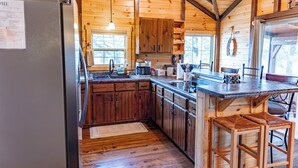 Une cuisine rustique aménagée dans une cabane en bois, comprenant un réfrigérateur, des placards en bois, un évier et un coin bar avec des tabourets.