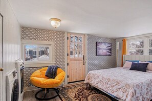 Un dormitorio con cama, una silla, un televisor y una puerta.