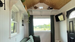 Una habitación acogedora con techo de madera, sofá verde, televisor montado en la pared y ventana con cortinas.