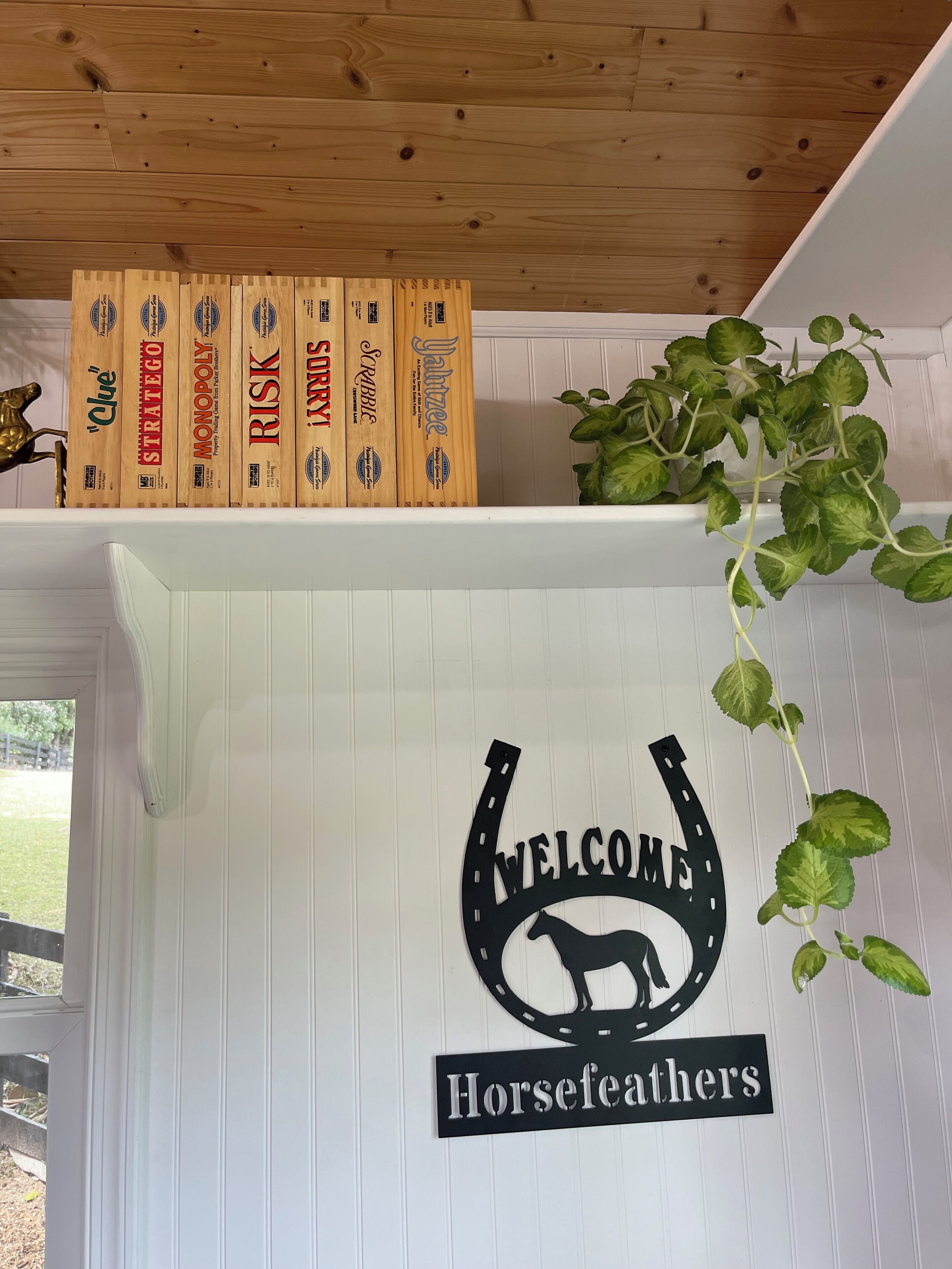 En velkomstskilt med en hestesilhuet og teksten "Welcome Horsefeathers" på en hvid væg.