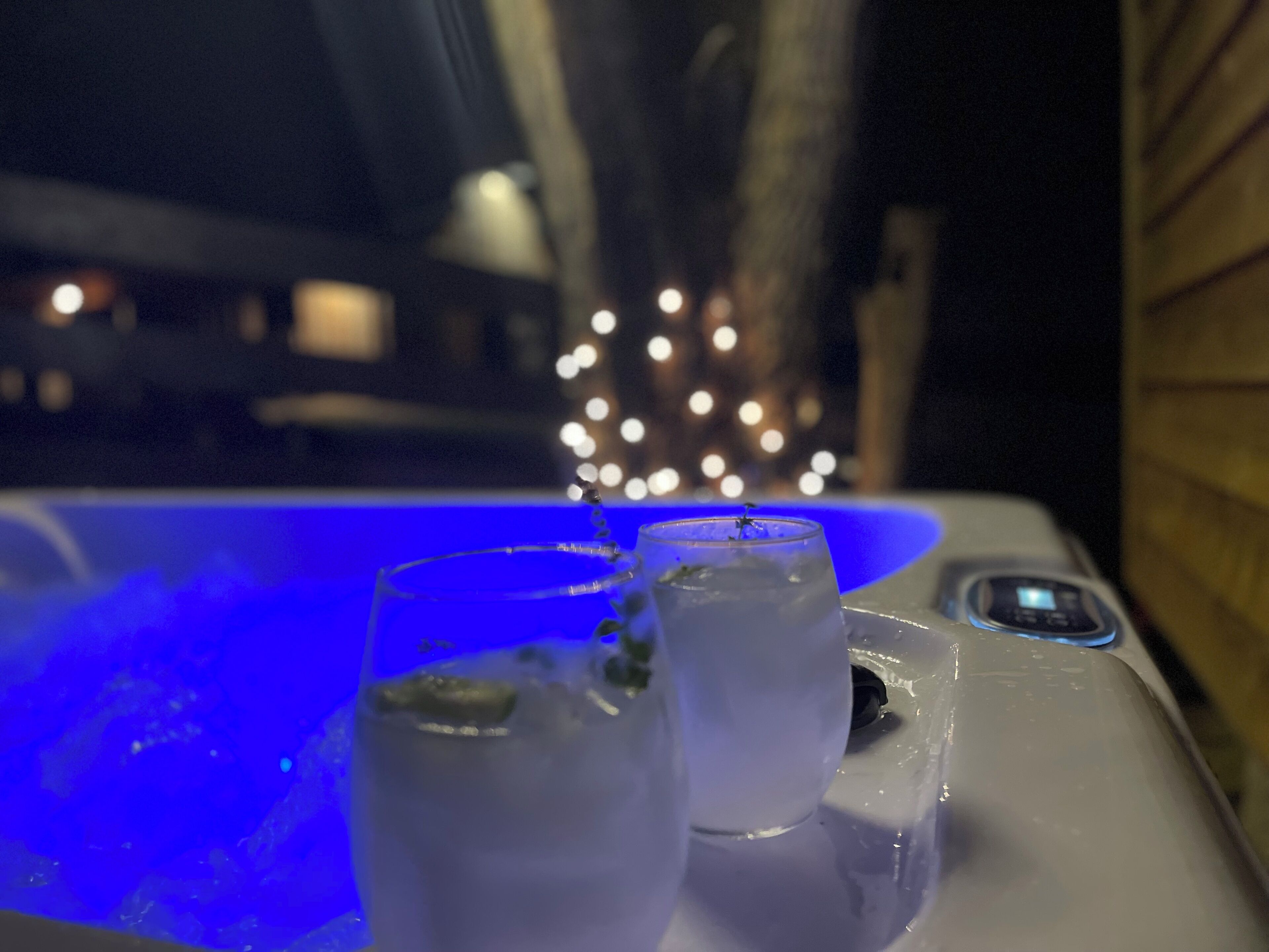 Un jacuzzi con dos vasos de agua, un panel de control y un fondo borroso con luces.