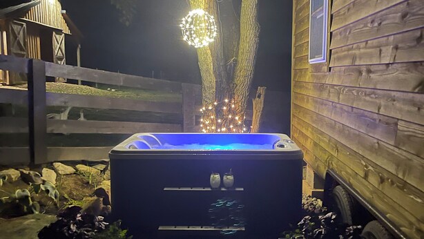 Un jacuzzi frente a una cabaña de madera con un árbol al fondo.