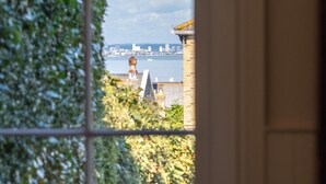 A view through a window with a view of a distant cityscape, including a prominent tower and a body of water. - Spacious, cosy 5 bedroom home in the village of Seaview on the Isle of Wight views across the solent (Seaview)