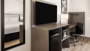 A hotel room with a bed, a flat-screen TV mounted on a wooden desk, a microwave, a black office chair, and a framed picture on the wall. - Clean 1 King-Bed Room in York just off I-83 Harrisburg Hershey (York)