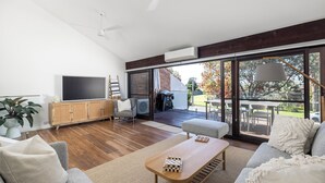 A spacious living room with a large TV, wooden cabinet, and comfortable seating. - Solace by the Bay (Corlette)
