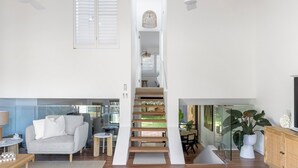 A spacious living area with a staircase leading to a second floor, a sofa, a small table, and a cabinet. - Solace by the Bay (Corlette)