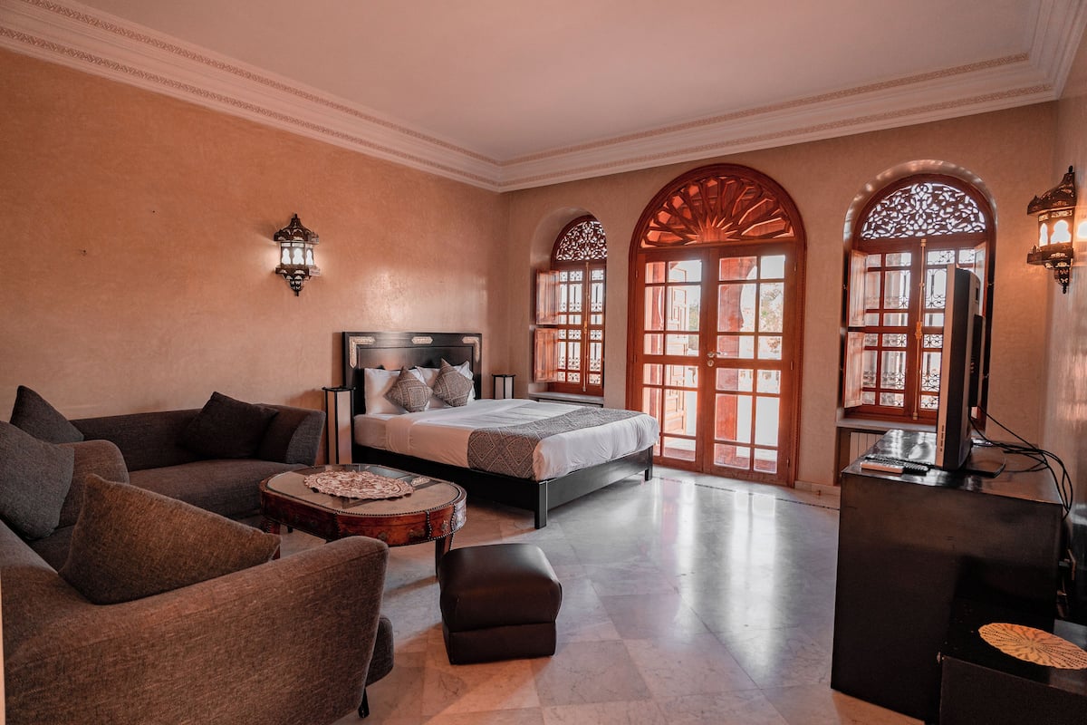 A spacious room with a bed, a sofa, a small round table, and a television.