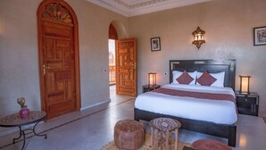 A hotel room with a large bed, two bedside tables with lamps, a small round table, and a decorative stool. - Abraj Bladi Resort (Marrakech)