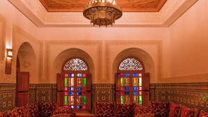An ornate room with intricate ceiling designs, a central glass-top table, and richly patterned sofas. - Abraj Bladi Resort (Marrakech)