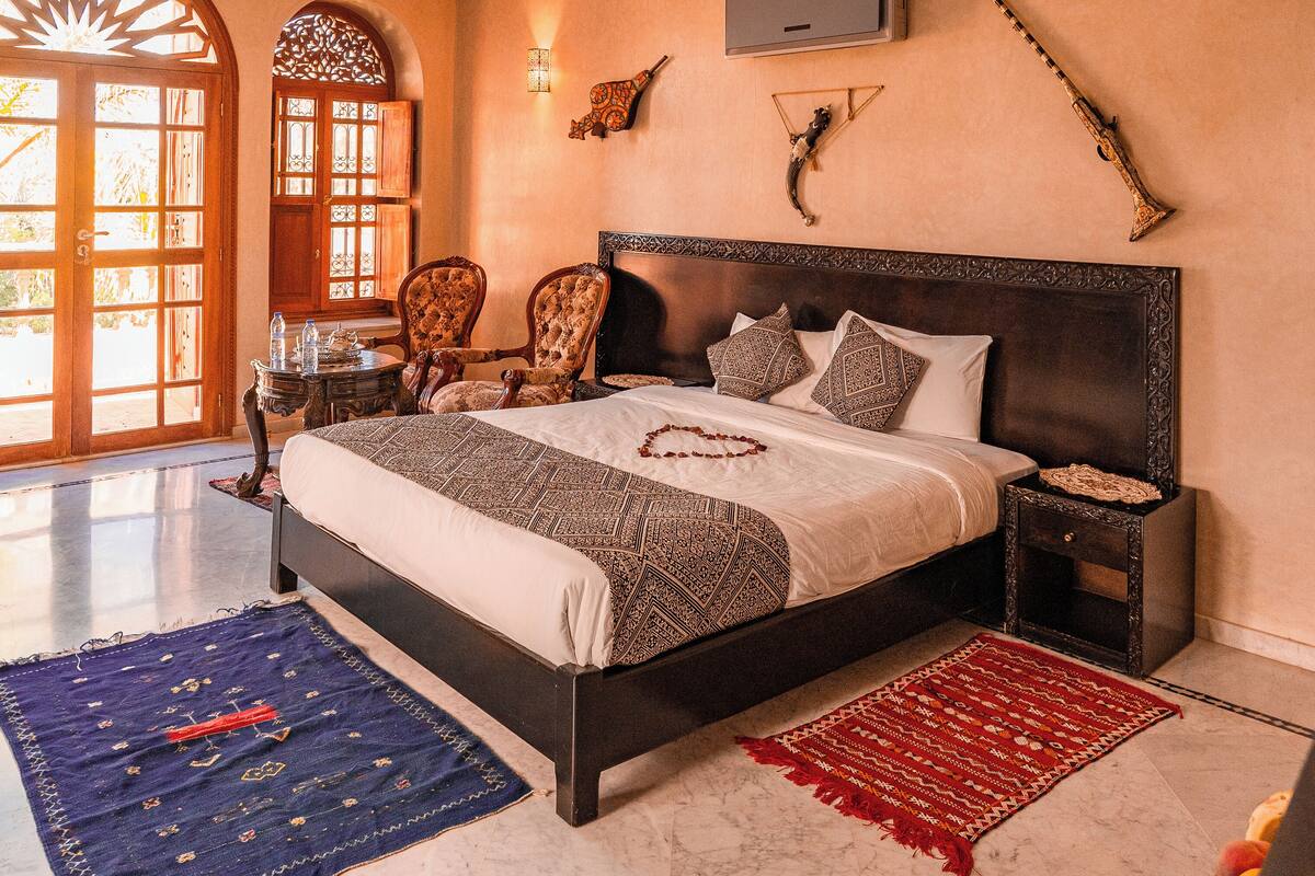 A spacious bedroom with a large bed, a nightstand, a TV, and a decorative wall piece.