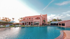 A swimming pool with lounge chairs and umbrellas, a building with arches, and a clear sky. - Abraj Bladi Resort (Marrakech)