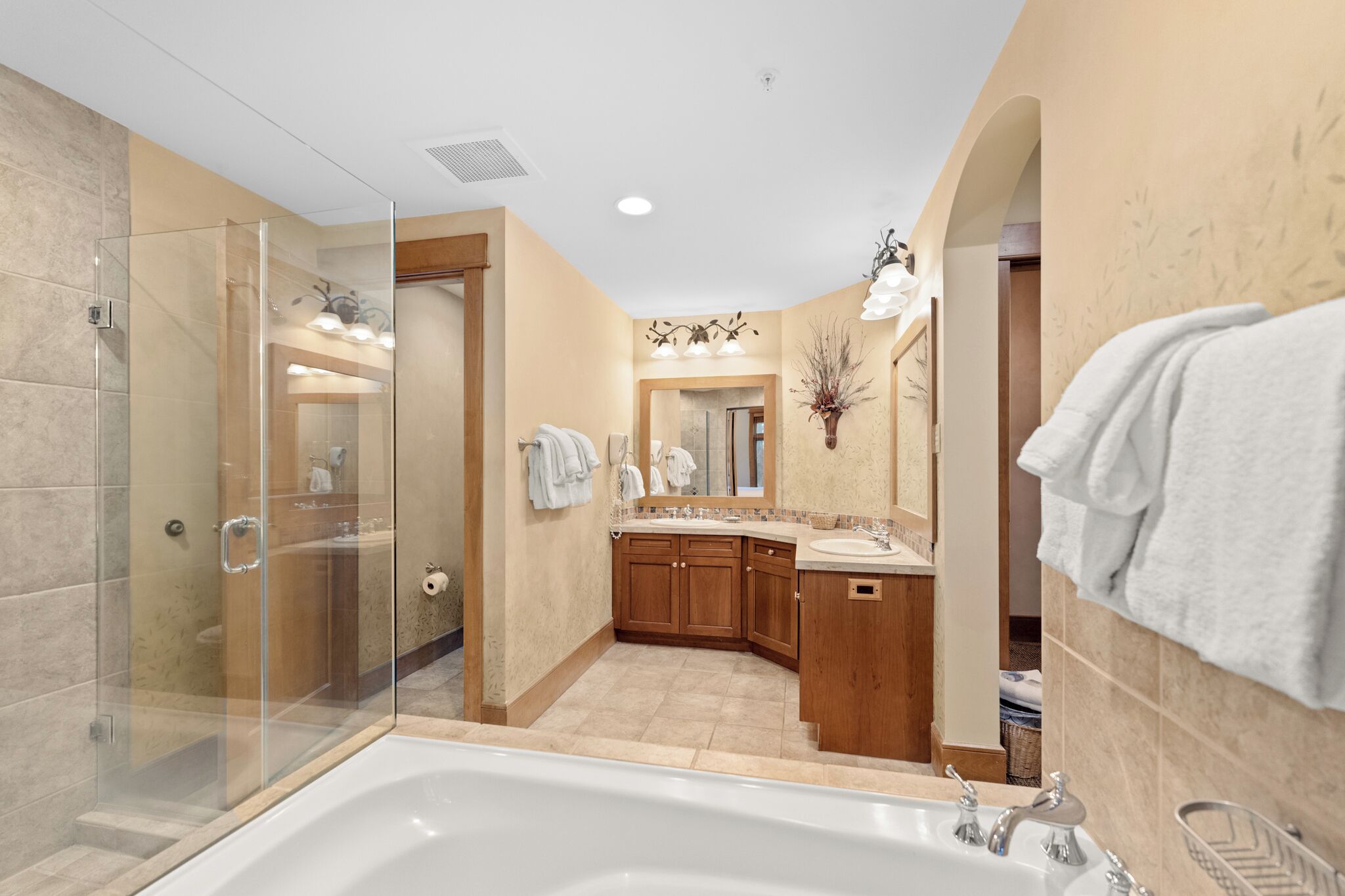 A modern bathroom with a glass-enclosed shower, a freestanding bathtub, wooden cabinetry, and a large mirror.