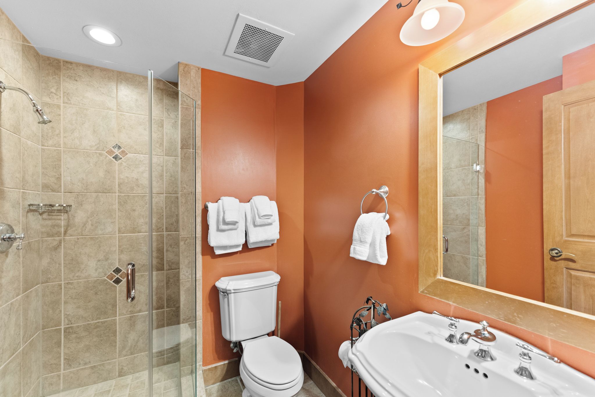 A bathroom with a glass-enclosed shower, a toilet, a sink with a mirror, and towels hanging on the wall.