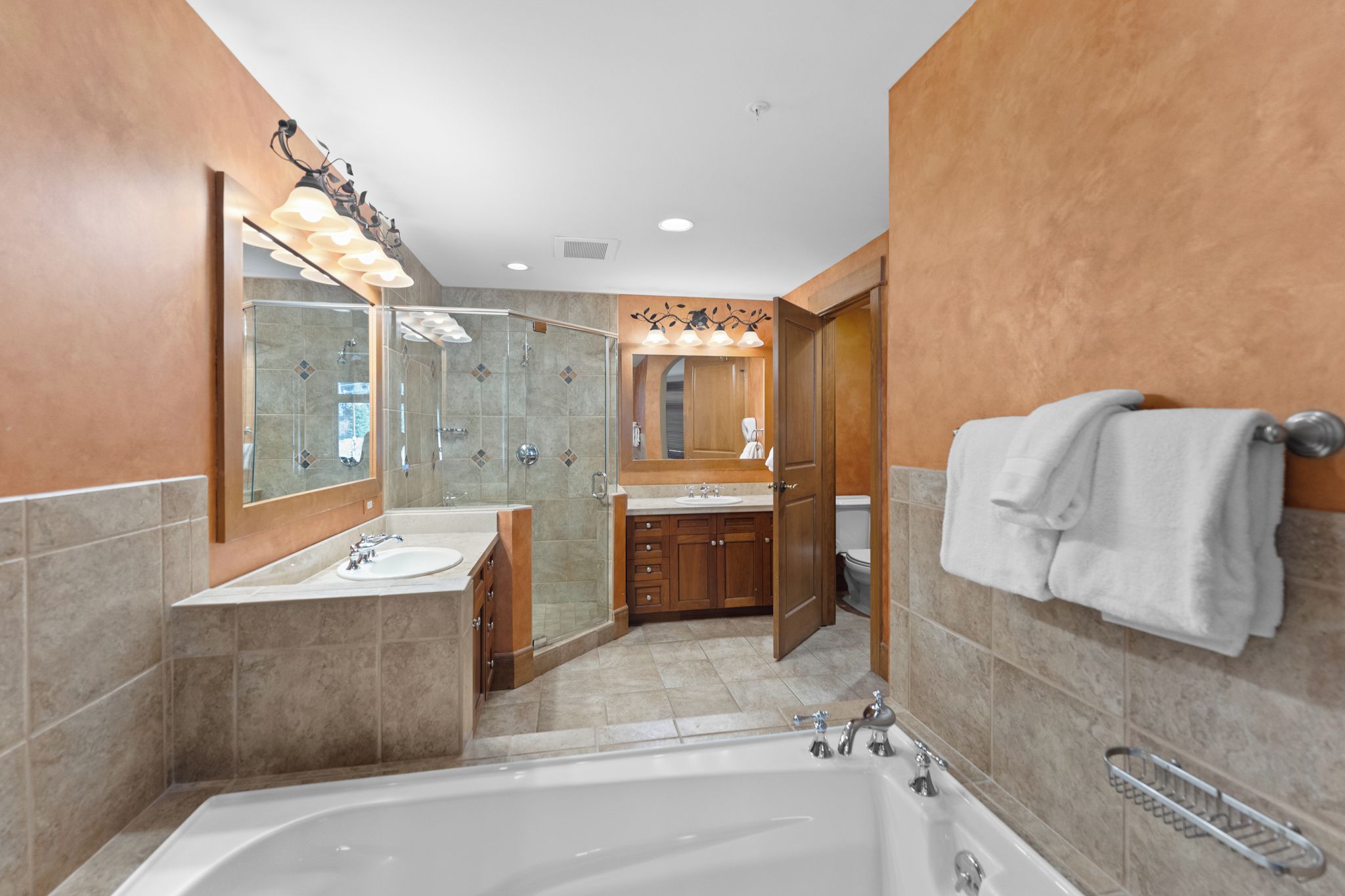 A modern bathroom with a large bathtub, a glass-enclosed shower, and wooden cabinetry.