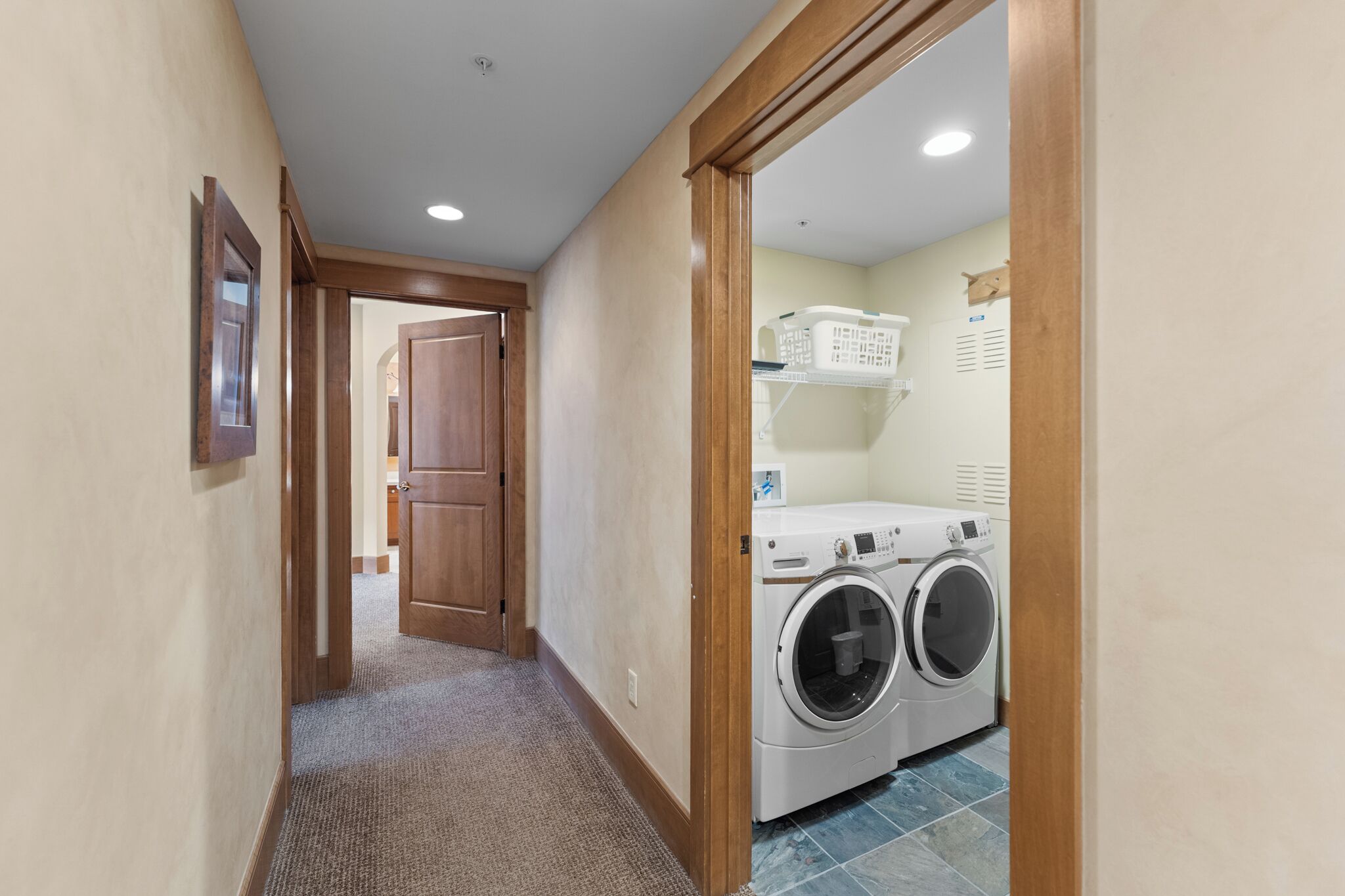 A laundry room with a front-loading washer and dryer, a drying rack, and a door leading to another room.