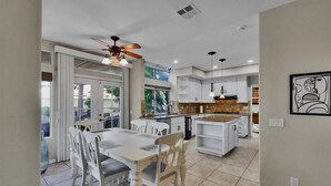 A modern kitchen with white cabinetry, a dining area with a white table and chairs, and a ceiling fan.