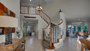 A spacious living area with a curved staircase, a wooden console table, and a chandelier.