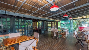 Un restaurante con mesas y sillas de madera, un espacio al aire libre cubierto y vistas a la vegetación.