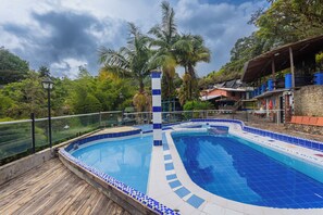 Une piscine dotée d’une terrasse en bois, entourée de palmiers et d’un mur en pierre.