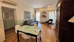 Un espace de vie compact comprenant un coin repas, un canapé, un fauteuil et des œuvres d’art accrochées aux murs.