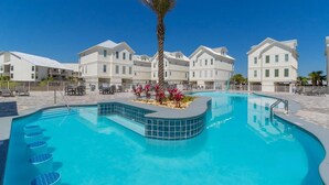 En swimmingpool med en palm och röda blommor i mitten, omgiven av vita byggnader med balkonger.