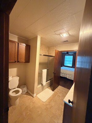 Een badkamer met toilet en douche, met een bed in de aangrenzende kamer.