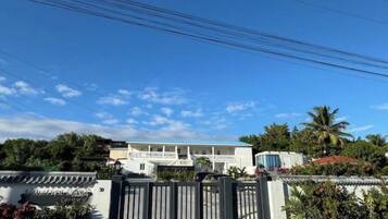 A gated entrance to a residential area with a white building and a blue-roofed structure in the background.