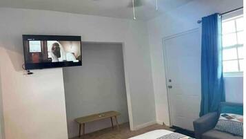 A hotel room with a bed, a bench, a television mounted on the wall, and a door with a blue curtain.