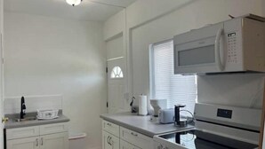 A kitchen with white cabinets, a microwave, an oven, and a window with blinds.