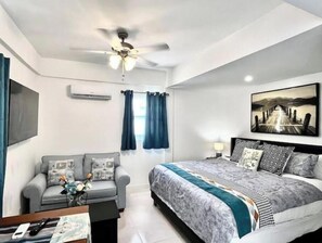 Un dormitorio moderno con cama, sofá, ventilador de techo y un cuadro en la pared.